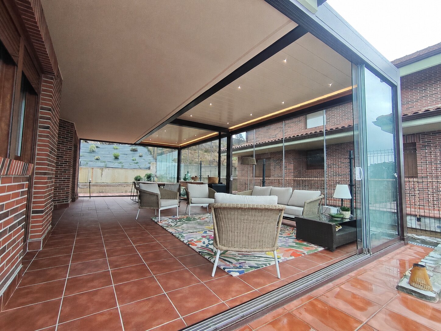 Porche acristalado con estructura de aluminio gris sobre una vivienda de piedra, con el campo al fondo
